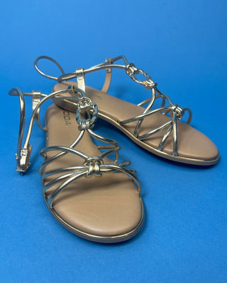 A pair of gold metallic strappy sandals with a tan footbed, against a solid blue background.