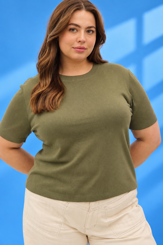 A woman wearing a short-sleeve crewneck knit top in olive green, paired with light beige pant