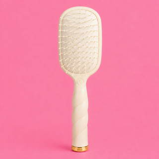 White paddle hairbrush with gold accents on a pink background