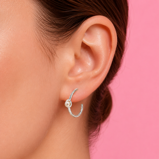 Close-up of an ear wearing a silver earring with a pearl on a pink background