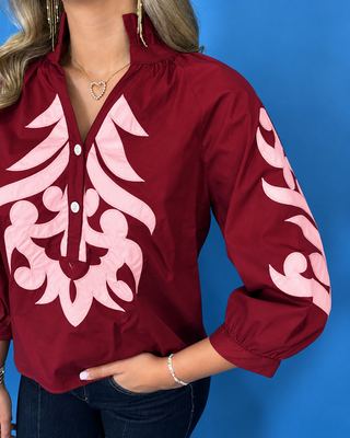 Rich ruby cotton top with blush embroidered appliqué, ruffle neckline, three-quarter balloon sleeves, and button placket.