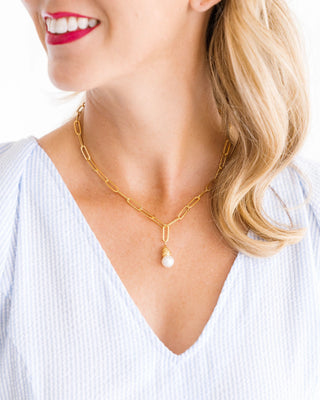 Gold chain necklace with a pearl pendant worn by a person against a white background