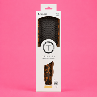 Packaged hair detangler brush with leopard print design on a pink background