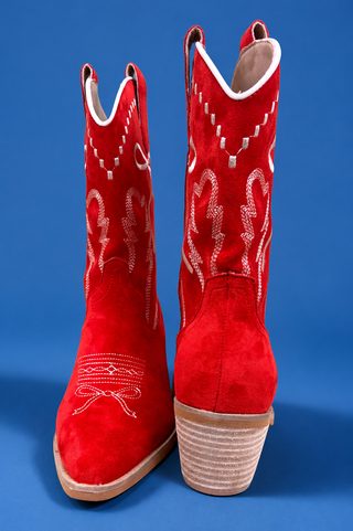 A pair of red suede cowboy boots with white embroidered western patterns, shown from the front and side against a so