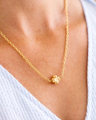 Gold necklace with a small pendant on a person wearing a light blue top.