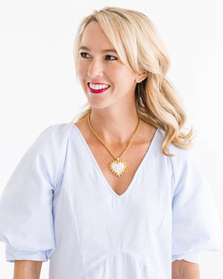 Woman wearing a gold necklace with a heart-shaped pendant on a white background