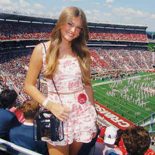 Woman in a floral dress at a football stadium with a large crowd and field.