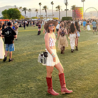 Woman in cowboy boots and hat at a music festival with palm trees and Ferris wheel in the background.
