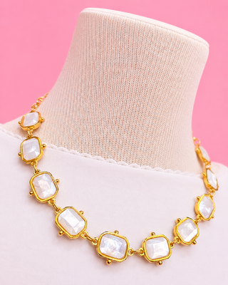 Gold necklace with large white stones on a mannequin against a pink background
