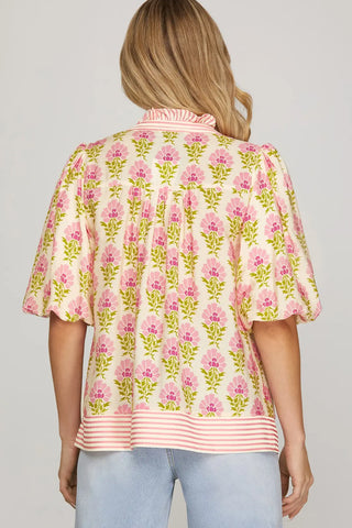 Woman wearing a floral blouse with pink flowers and green leaves on a plain background