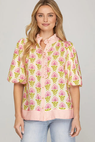 Woman wearing a floral blouse with pink and yellow flowers on a plain background