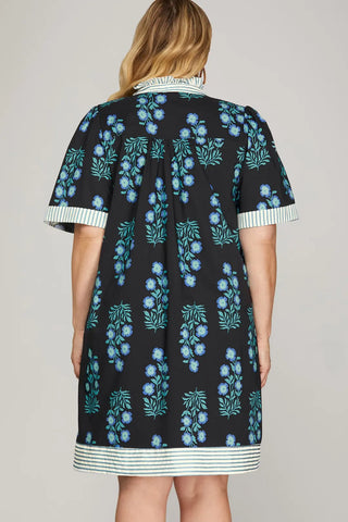 Woman wearing a black dress with blue floral pattern on a plain background