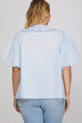 Person wearing a light blue blouse with ruffled sleeves on a plain background