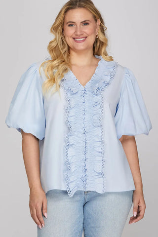 Woman wearing a light blue blouse with ruffled details and jeans on a plain background