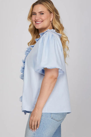 Woman wearing a light blue blouse with ruffled sleeves on a plain background