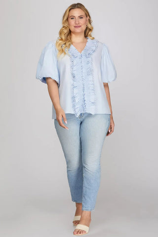 Woman wearing a light blue blouse with ruffled details and light blue jeans on a plain background