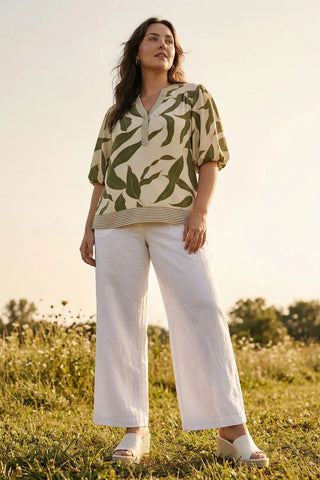 Woman wearing a patterned shirt and white pants standing in a field.