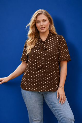 Woman wearing a brown polka dot shirt and blue jeans against a blue background
