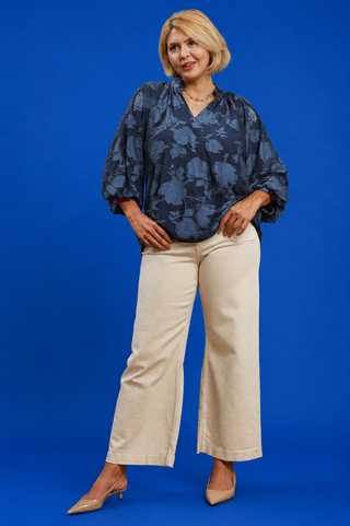 Woman wearing a blue floral blouse and beige pants against a blue background