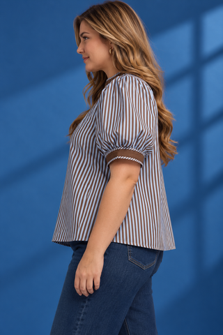 A woman modeling a short-sleeve button-up shirt with vertical blue and white stripes, brown trim