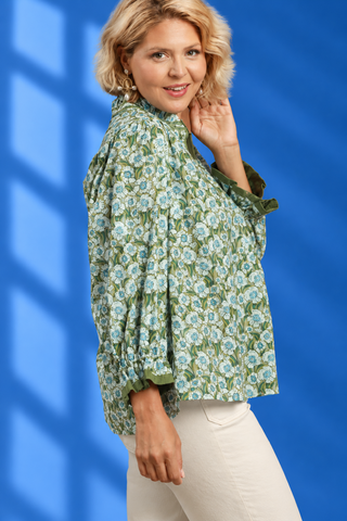 A woman wearing a green floral long-sleeve blouse with white pants