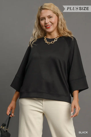 Woman wearing a black plus-size sweatshirt and beige pants against a gray background