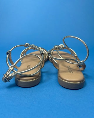 A pair of gold metallic strappy sandals with a tan footbed, against a solid blue background.