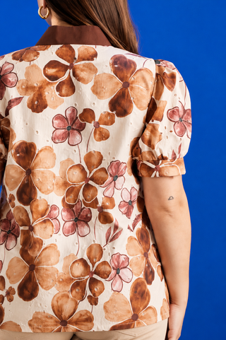 A woman wearing a short-sleeve blouse with a brown and pink floral watercolor pattern on a cream background