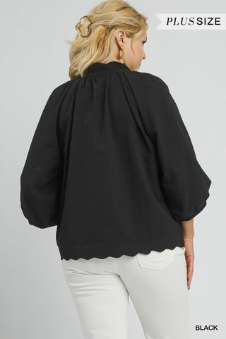 Woman wearing a black blouse with scalloped hem on a gray background