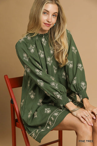 Woman wearing a green dress with floral patterns sitting on a red chair against a beige background