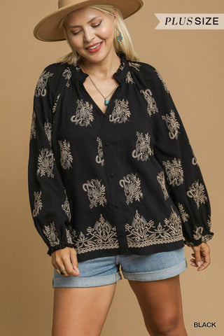 Woman wearing a black blouse with gold patterns and denim shorts on a beige background