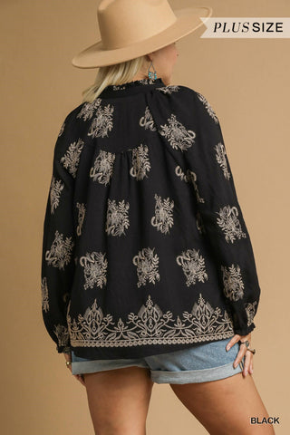 Person wearing a black blouse with white patterns and denim shorts on a beige background