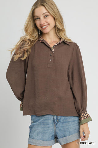Woman wearing a brown long-sleeve shirt with patterned cuffs and collar, paired with denim shorts on a white background.
