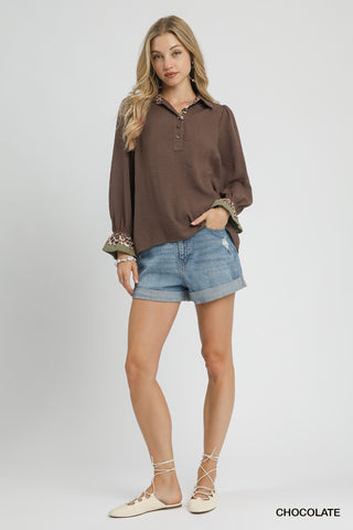 Woman wearing a brown long-sleeve top and denim shorts on a gray background