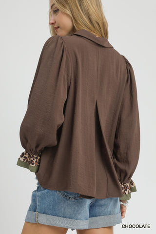 Brown blouse with leopard print cuffs worn by a person on a white background