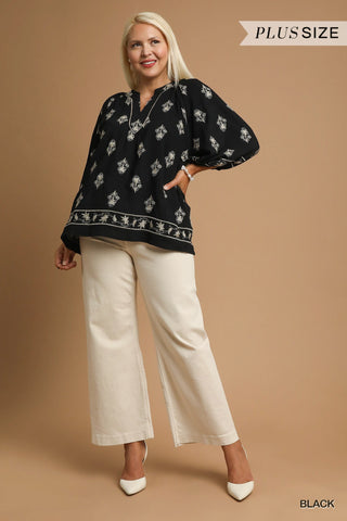 Woman wearing a black patterned top and white pants on a beige background