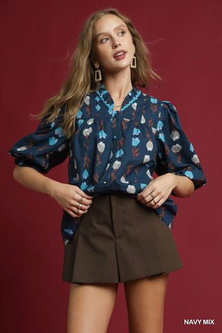 Woman wearing a navy blouse with colorful patterns and brown shorts against a red background