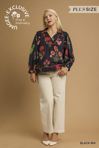 Woman wearing a floral blouse with beige pants on a brown background, featuring Umgee Exclusive branding.