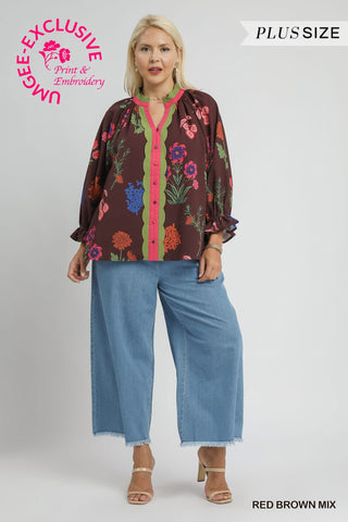 Woman wearing a plus-size floral blouse and jeans with UMGEE Exclusive branding.