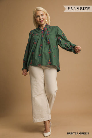 Woman wearing a green blouse with floral patterns and beige pants on a brown background