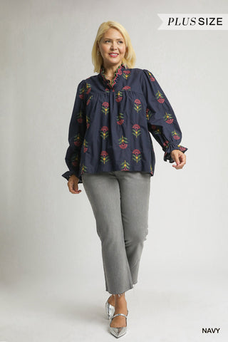 Woman wearing a navy blouse with floral embroidery and gray pants on a white background