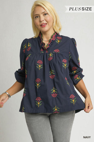 Woman wearing a navy blue blouse with floral embroidery on a plain background