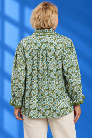 A woman viewed from the back wearing a green long-sleeve blouse with a dense white and light blue floral print,