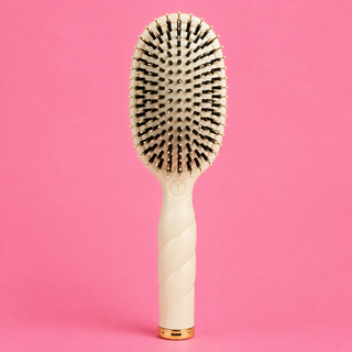 Hairbrush with a white handle and gold accents on a pink background