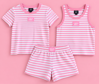 A children's two-piece pajama set laid flat on a pink background, including a short-sleeve striped shirt and matching shorts, with a sleeveless striped tank top also shown. The set has pink and white horizontal stripes, pink trim, and a small pink chest patch reading 'LULU MAC'.