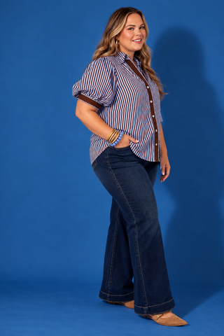 A woman modeling a short-sleeve button-up shirt with vertical blue and white stripes, brown trim