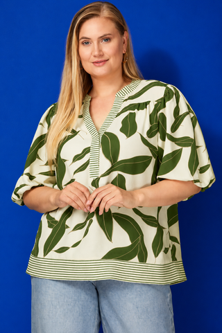 Woman wearing a green and white leaf-patterned blouse against a blue background