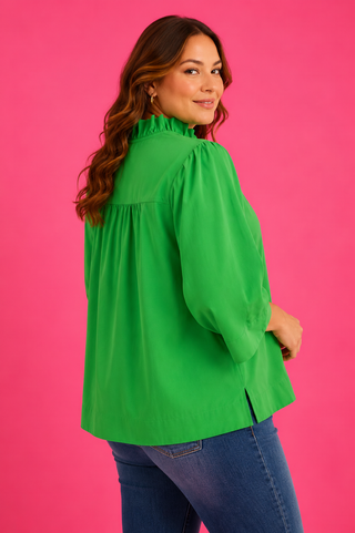 Woman wearing a green blouse and blue jeans against a pink background