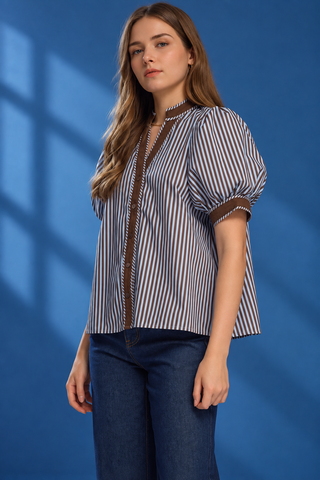 A woman modeling a short-sleeve button-up shirt with vertical blue and white stripes, brown trim