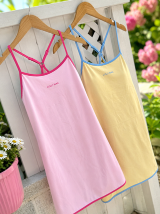 Two sleeveless camisole-style nightgowns hang on wooden hangers against a white wooden fence outdoors. The front nightgown i